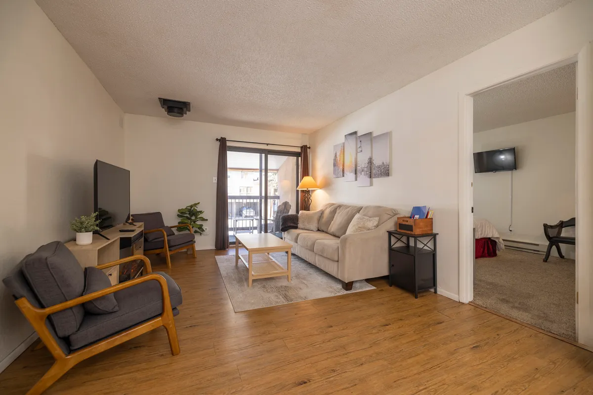 A cozy living space with a sofa, coffee table, television, and wall artwork. Sunlight spills in, creating an inviting mood. The arrangement is perfect for relaxing or entertaining, with a focus on comfort and shared experiences.